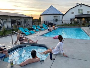A swimming pool area with lounge chairs, a hot tub, and a building in the background.