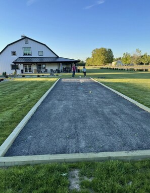 A courtyard with a croquet field, a white building with a dark roof, and a grassy area with trees.