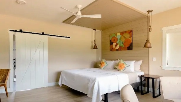 Quarto com cama, ventilador de teto, um quadro e janela.