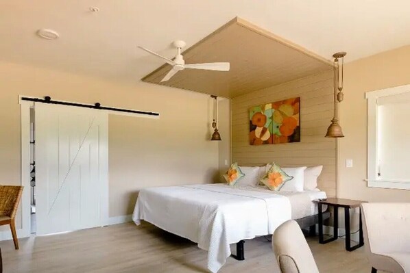 A bedroom with a bed, a ceiling fan, a painting, and a window. - Barrel Suite at The Barn | Boutique Hotel (Walla Walla)