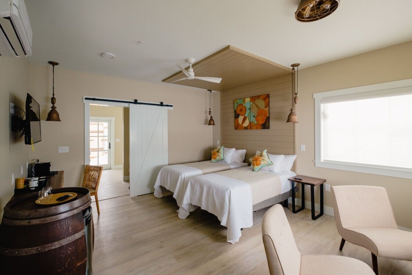 Une chambre avec deux lits, un ventilateur de plafond, une fenêtre et un tonneau en bois.