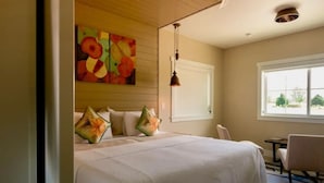 Quarto de hotel com uma cama grande, um quadro na parede, janela com vista e uma cadeira.