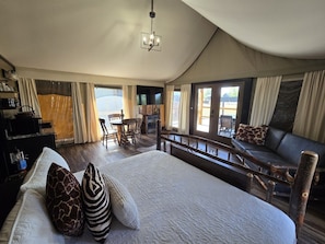 A spacious bedroom with a large bed, a wooden headboard, a seating area with a sofa and chairs, and a balcony with curtains.