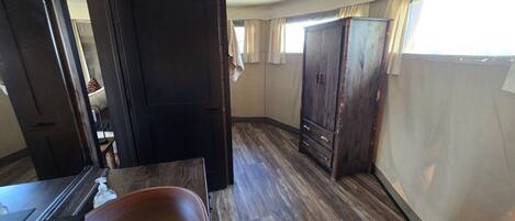 Ein Zimmer mit Holzboden, einem dunklen Holzschrank und einer Tür zu einem weiteren Raum.