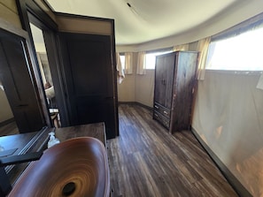 A room with a wooden floor, a dark wooden cabinet, and a door leading to another room.