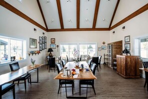 A spacious dining area with a long wooden table, multiple chairs, and a high ceiling with exposed beams. - Loess Suite at The Barn | Boutique Hotel (Walla Walla)