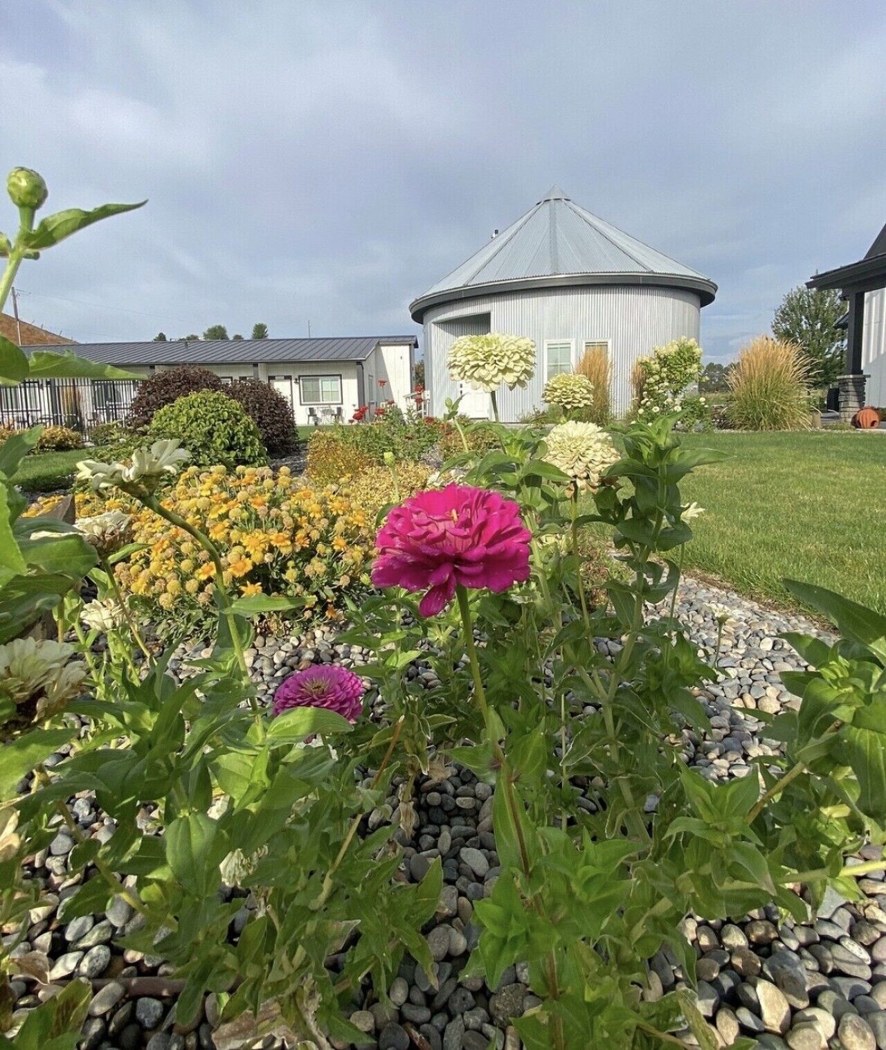 Un giardino con diverse fioriture e un edificio a tetto curvo sullo sfondo.