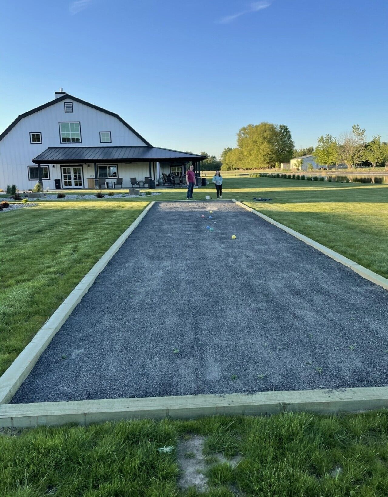 Une cour avec un terrain de croquet, un bâtiment blanc doté d’un toit sombre et une zone herbeuse parsemée d’arbres.