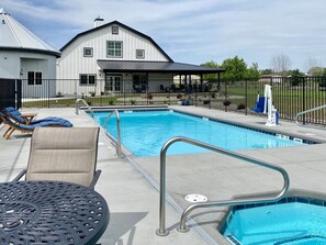 A swimming pool with lounge chairs and a covered seating area, surrounded by a fence. - Loess Suite at The Barn | Boutique Hotel (Walla Walla)