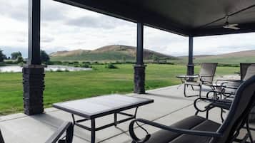 Une terrasse couverte avec une table et des chaises, un ventilateur de plafond et une vue sur un champ verdoyant et des collines.