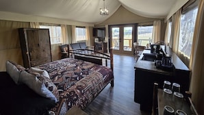 A tented accommodation with a bed, desk, and chairs.