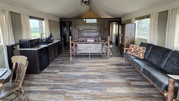 A tented accommodation with a central bed, a sofa, a dining area, and a kitchenette.