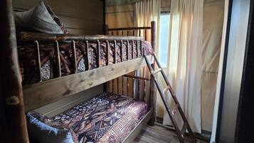 Ein Stockbett mit gemusterten Betttextilien, einer Holzleiter und einem Fenster mit Vorhängen.