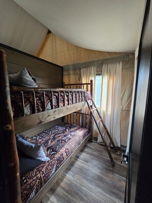 Una cama individual con ropa de cama estampada, una escalera de madera y una ventana con cortinas.
