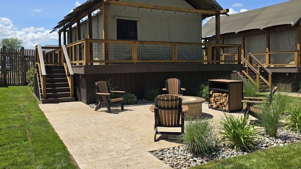 A two-story building with a covered patio area, outdoor seating, and a wooden deck. - Watusi Luxury Tent #1 (Chittenango)