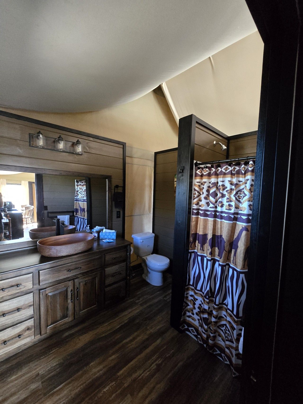 Un baño con tocador de madera, un espejo grande, inodoro y cortina de ducha con diseño estampado.