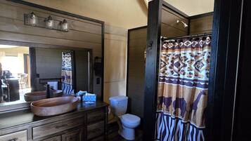 Un baño con tocador de madera, un espejo grande, inodoro y cortina de ducha con diseño estampado.