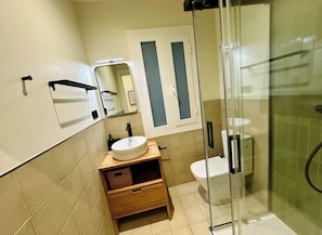 Ein modernes Badezimmer mit einer Duschkabine aus Glas, einem weißen Waschbecken und einer Toilette.