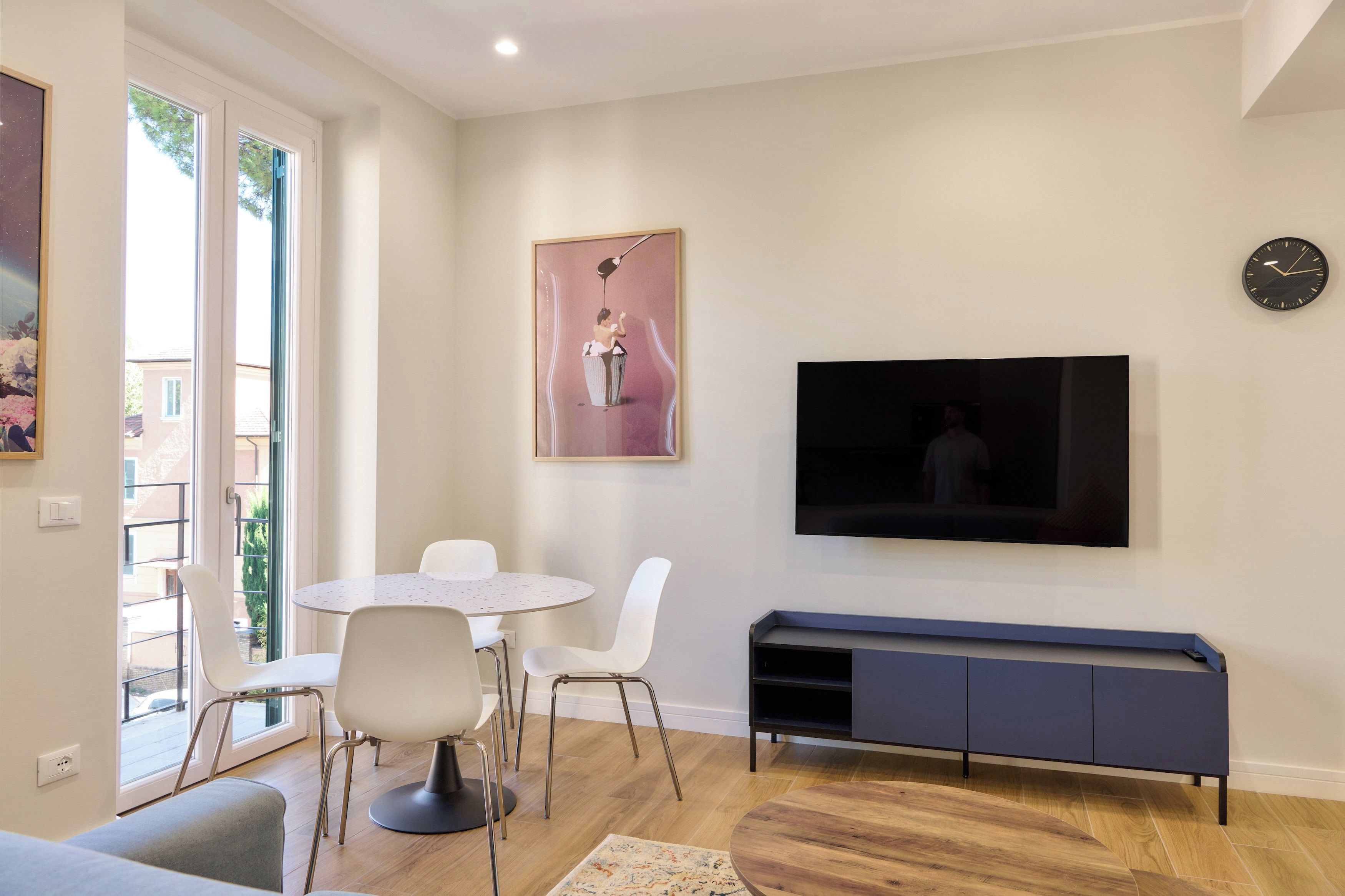 Ein modernes Wohnzimmer mit einem runden Esstisch, weißen Stühlen, einem Wand-Fernseher und einer Bank.