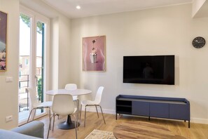 Ein modernes Wohnzimmer mit einem runden Esstisch, weißen Stühlen, einem Wand-Fernseher und einer Bank.