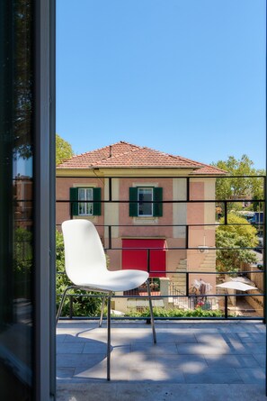 A white chair on a balcony with a view of a building with a red door and green shutters. - Casa e Appartamento Vacanze Gallese 12 (Roma)