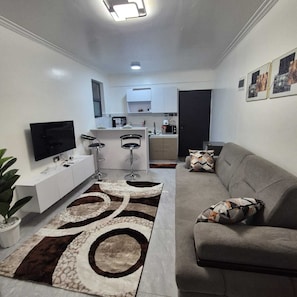 A modern living room with a grey sofa, a flat-screen TV, and a patterned rug. - Cozy Air BNB 2BR-Fast WiFi (Nairobi)