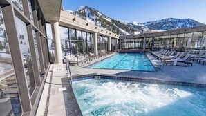 Piscina com cadeiras de descanso e montanhas ao fundo.