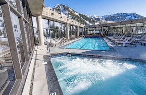 Piscina con sillas de descanso y montañas al fondo.