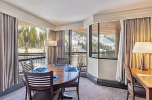 Habitación de hotel con una gran mesa de comedor, sillas, una lámpara y vistas a un paisaje montañoso nevado.