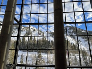 Une vue à travers une fenêtre à carreaux, qui révèle un paysage montagneux enneigé, avec des arbres et un ciel dégagé.
