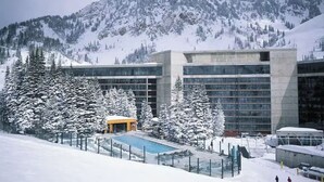 Um hotel moderno com área de piscina, rodeado por árvores cobertas de neve e montanhas.