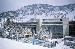 Un hotel moderno con zona de piscina, rodeado de árboles nevados y montañas.