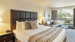 Quarto de hotel com uma cama grande, um sofá, uma mesa pequena, uma mesa de cabeceira e uma varanda com vista.