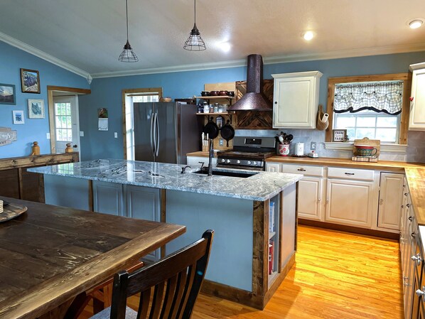 A kitchen with a central island, stainless steel appliances, wooden flooring, and a dining area with a table and chairs.