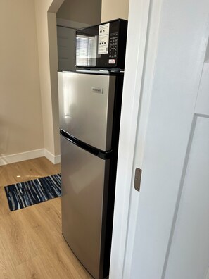 A stainless steel refrigerator with a built-in microwave, located in a kitchen with wooden flooring and a white door. - Tiny House 1 bed in Council Bluffs Iowa, 1 mile from downtown Omaha! (Council Bluffs)