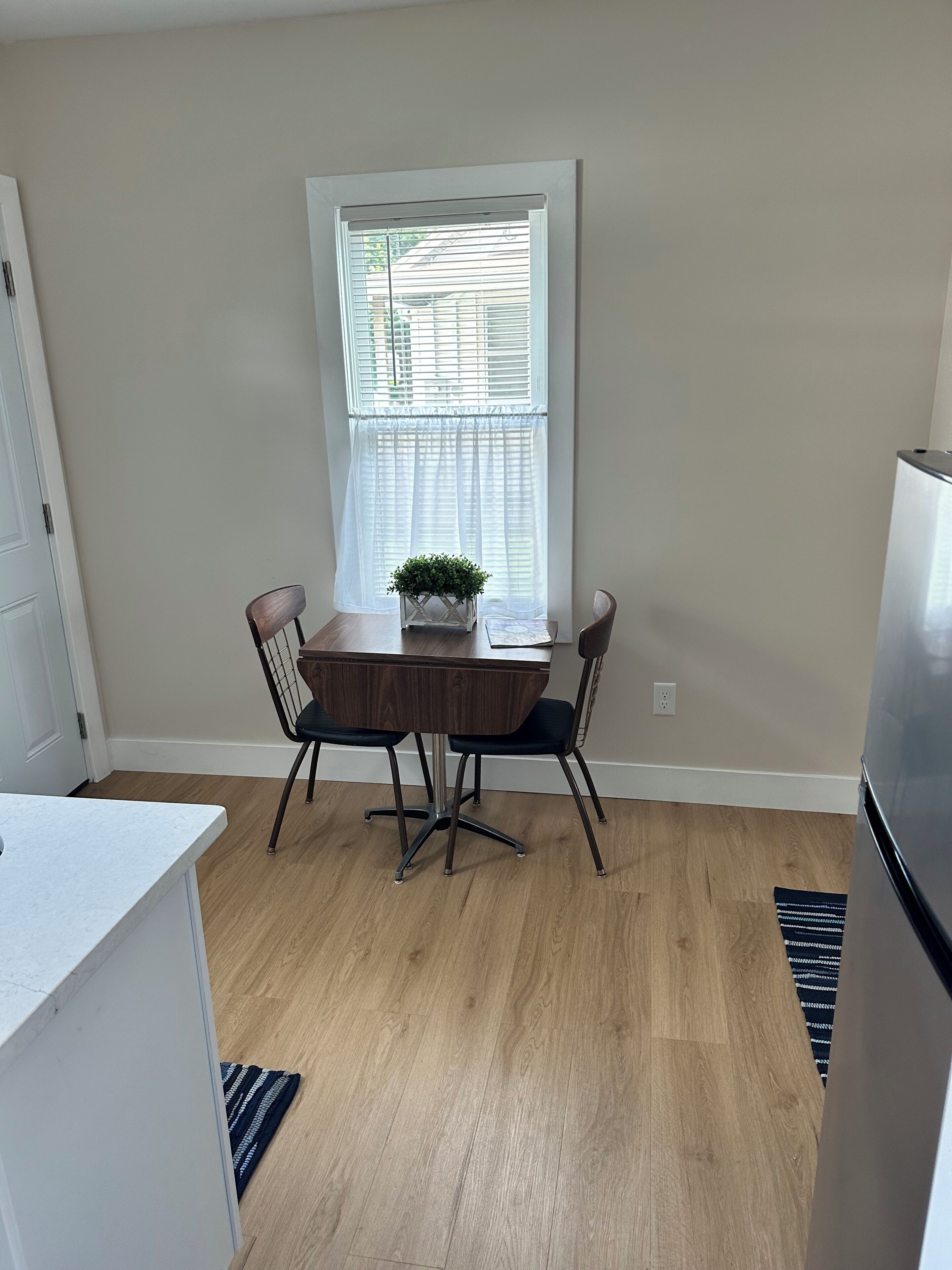 A kitchen with a dining table, chairs, a refrigerator, and a window with blinds.