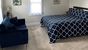 Quarto com teto inclinado, cama com colcha estampada em padrão geométrico, sofá azul escuro, duas obras de arte penduradas na parede e um ventilador de teto.