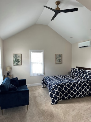 Una camera da letto con soffitto spiovente, un letto con copripiumino a motivi geometrici, un divano blu scuro, due opere d'arte appese al muro e una ventola a soffitto.