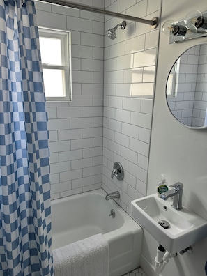 Un bagno con una vasca, un lavabo, una doccetta, una finestra e uno specchio.