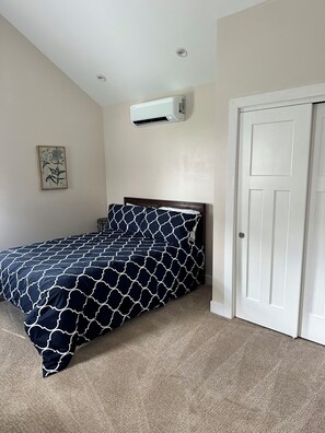 Una camera da letto con un letto, un condizionatore d'aria, una porta e un quadro appeso al muro.