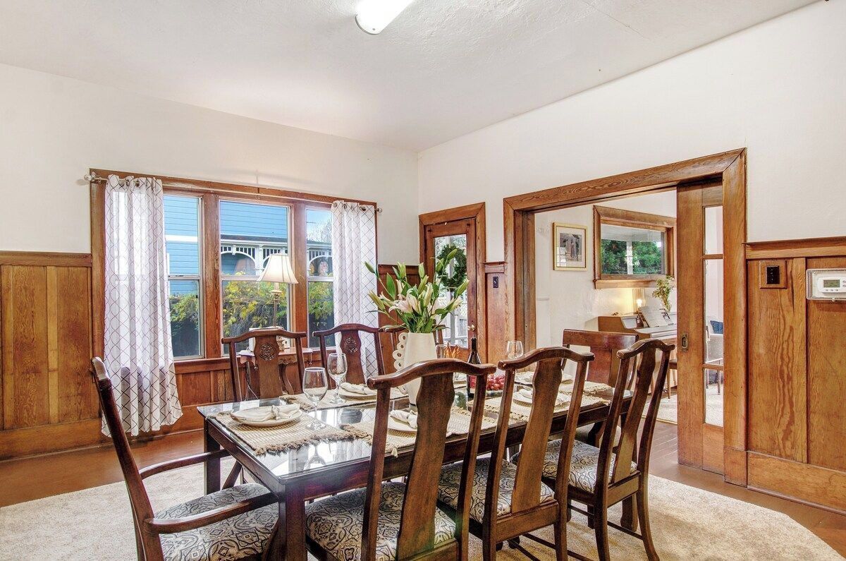 A dining room with a wooden table and chairs, a vase with flowers, and a view through the window.