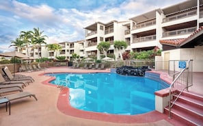 Area piscina di un hotel con lettini, una piscina e un edificio a più piani con balconi.