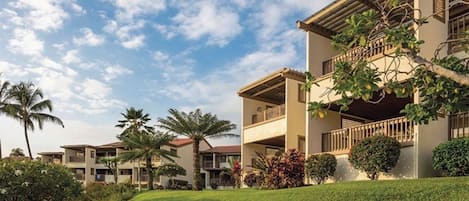 A multi-story hotel with a flat roof, balconies, and a well-maintained lawn.