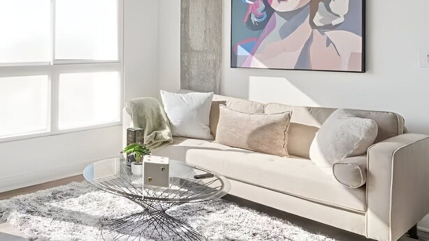 Uma sala de estar moderna com um sofá bege, uma mesa de centro de vidro e uma grande pintura abstrata na parede.