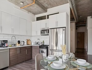 Een moderne keuken met witte kasten, roestvrijstalen apparatuur en een eethoek met een glazen tafel voor vier personen.