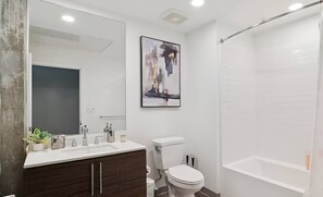 Een moderne badkamer met een wit wastafel, een donker houten opbergmeubel, een toilet, een douche met glazen deur en een grote spiegel.