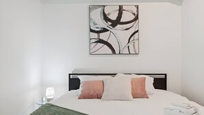 Uma cama bem arrumada com cabeceira, um quadro abstrato na parede e um abajur.