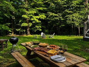 Ein Essbereich im Freien mit einem Picknicktisch, der für eine Mahlzeit gedeckt ist, umgeben von üppigem Grün und Bäumen.