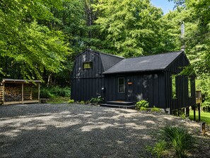 Eine schwarze Holzhütte mit einem Schotterweg und einem Holzgebäude zur linken Seite.