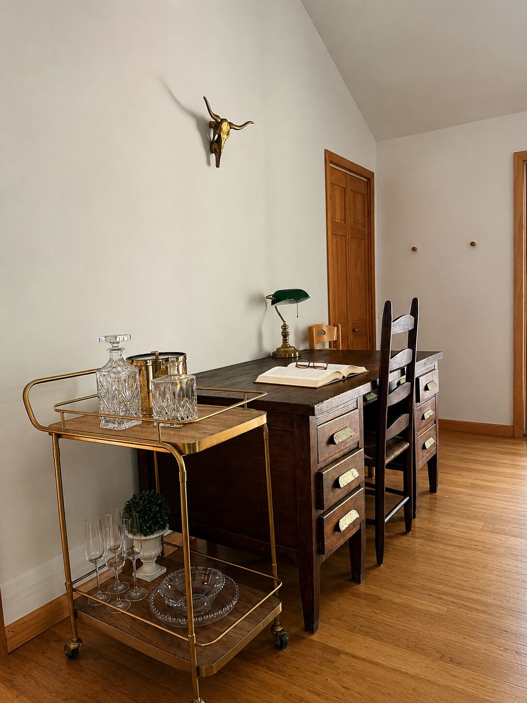 Un coin repas avec une table en bois, des chaises, un chariot doré contenant de la verrerie et un crâne de vache accroché au mur.